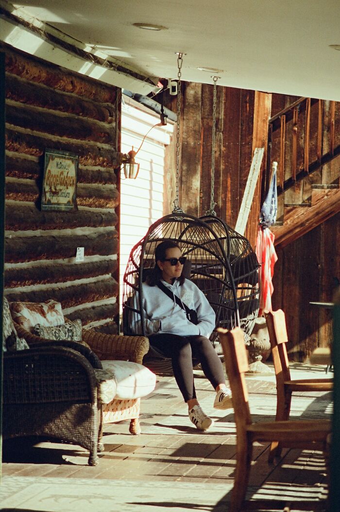 Person wearing sunglasses sitting on a hanging chair in a rustic room, relaxing after drunk fumbles and bad decisions.