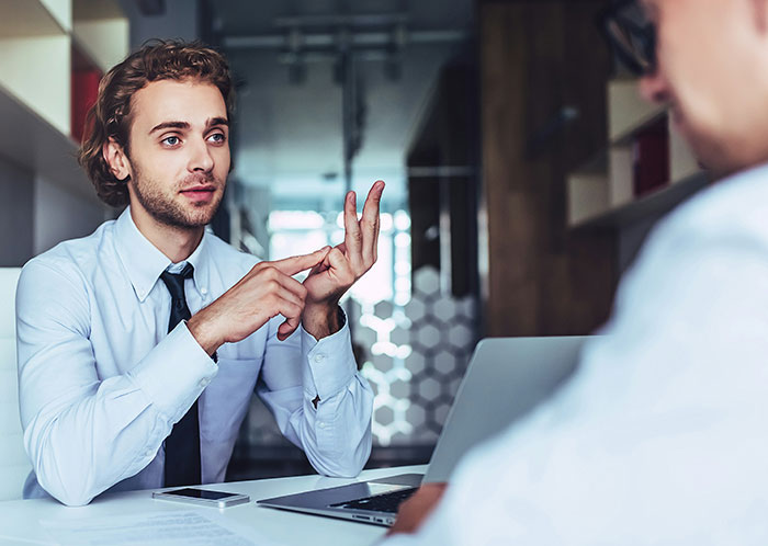 Man in office explaining something with hand gestures to new colleague during a language misunderstanding discussion.