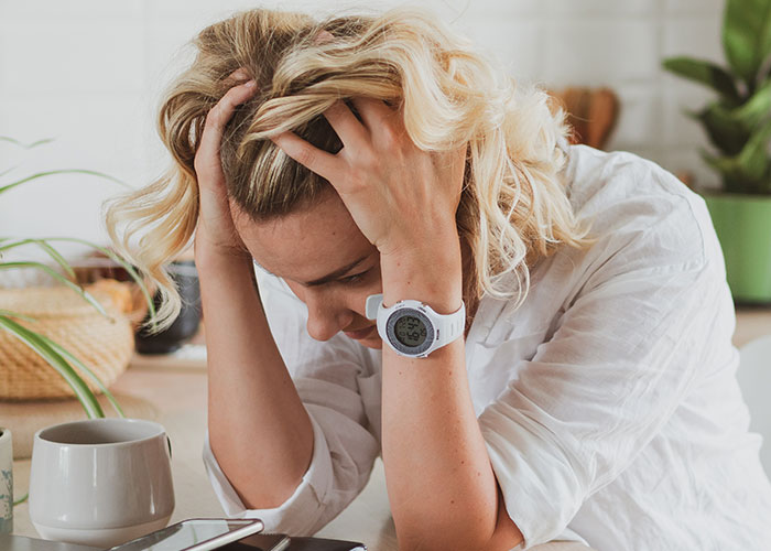 Stressed woman holding her head in her hands, representing danger caused by monster-in-law in a home setting.