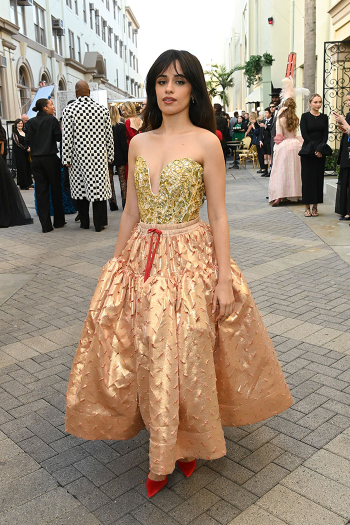 Female celebrity at Vogue World Hollywood 2025 wearing a gold and peach textured dress with red heels at an outdoor event.