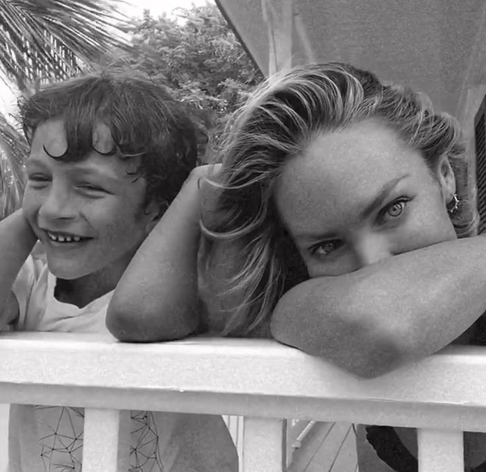 Victoria&rsquo;s Secret model resting on railing with child, black and white image showing a candid moment outdoors.
