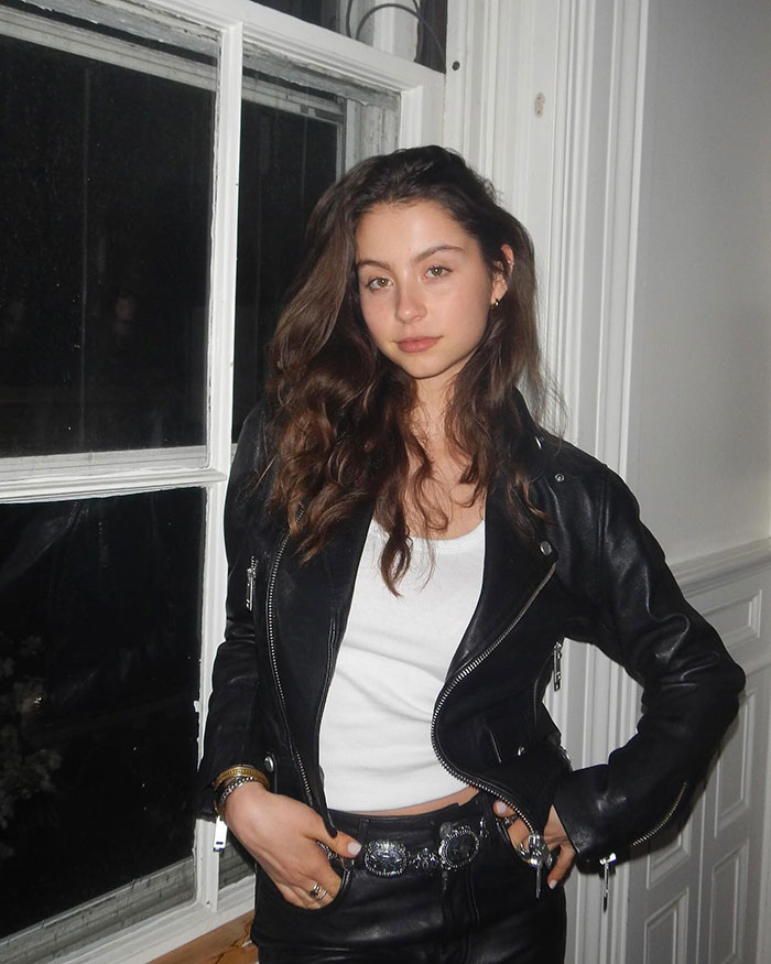 Young woman posing indoors wearing a vintage leather jacket and belt, embodying timeless elegance and vintage fashion at a gala.