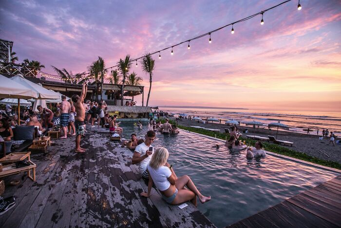 People relaxing by an infinity pool at sunset during a social gathering with a beach in the background near-death experiences theme.
