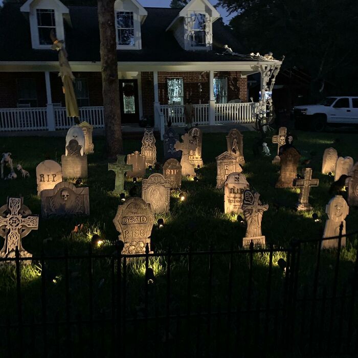 Outdoor Halloween decorations featuring a spooky illuminated graveyard display with tombstones and skeletons at night.