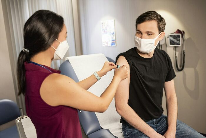 Healthcare worker administering vaccine to young man wearing a mask, highlighting gender roles in unfair relationships.