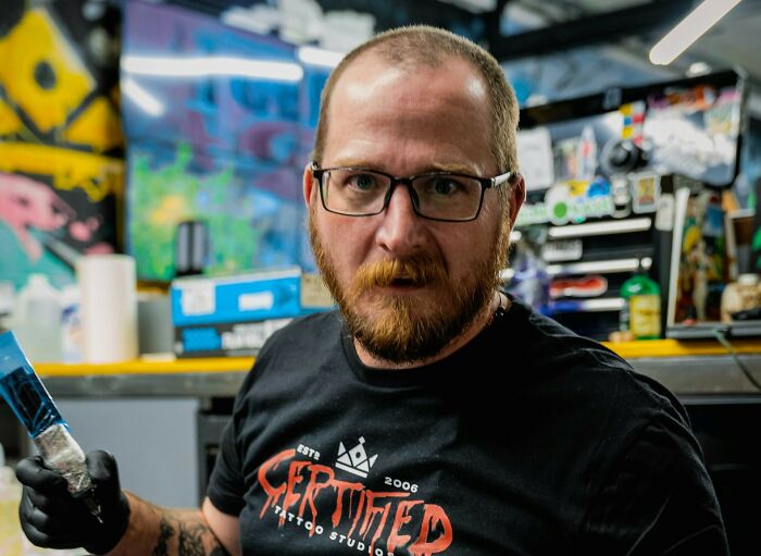 Tattoo artist with glasses in a studio holding a tattoo machine, representing tattoo artists messing up their work.