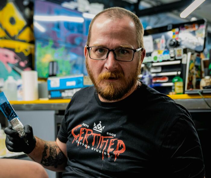 Tattoo artist holding a tattoo machine in a colorful studio, representing strange and offensive tattoo artists.