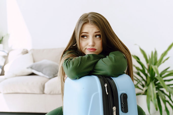 Woman visiting friend abroad looking worried and leaning on suitcase, considering escape after intoxicated partner serenade.