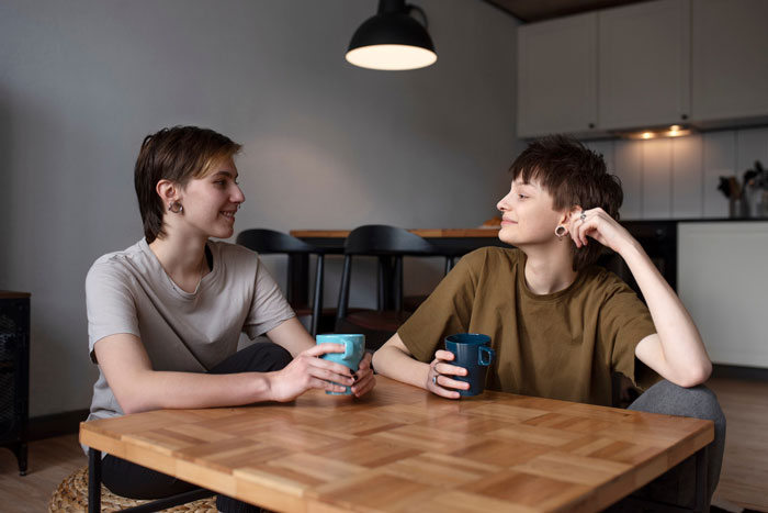 Two friends visiting abroad, sitting at a table with coffee, discussing concerns about an intoxicated partner's behavior.