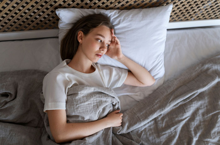 Young woman lying in bed looking worried, representing a lady visiting friend abroad considering escape after intoxicated partner's serenade.