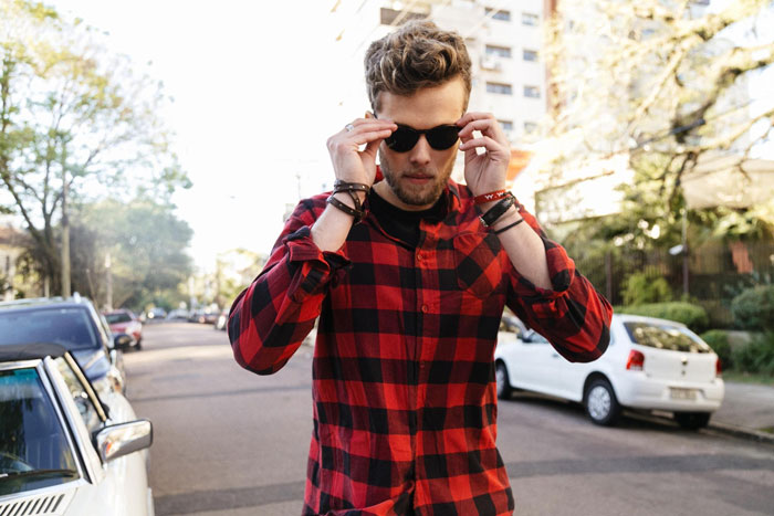 Young man in red plaid shirt putting on sunglasses on a city street, illustrating rich guy trying to rip off widow.