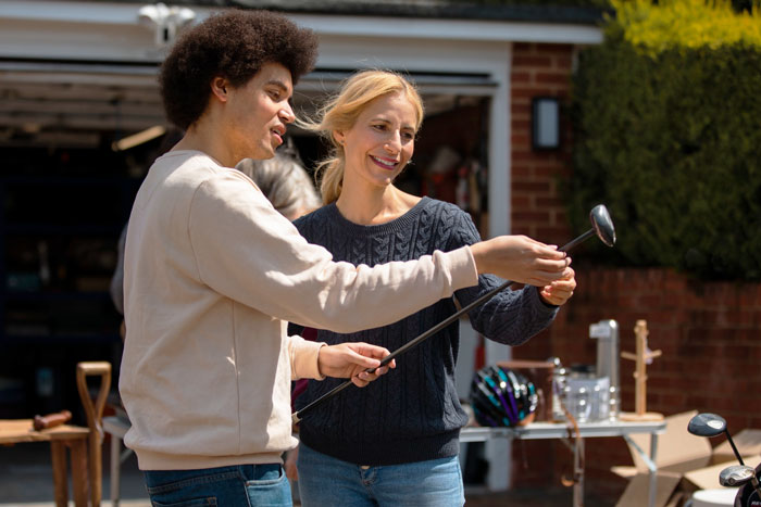 Young man and woman examining golf clubs outside, illustrating rich guy trying to rip off widow by lowballing golf club price.