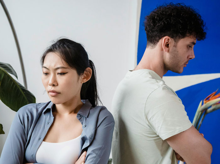 Two young adults back to back, looking upset, illustrating conflict over rent and mooching off cousin.