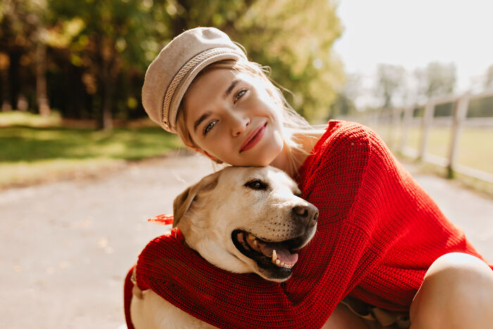 Woman wearing a hat and red sweater hugging her intelligent pet dog outdoors, showcasing surprising pet behavior.
