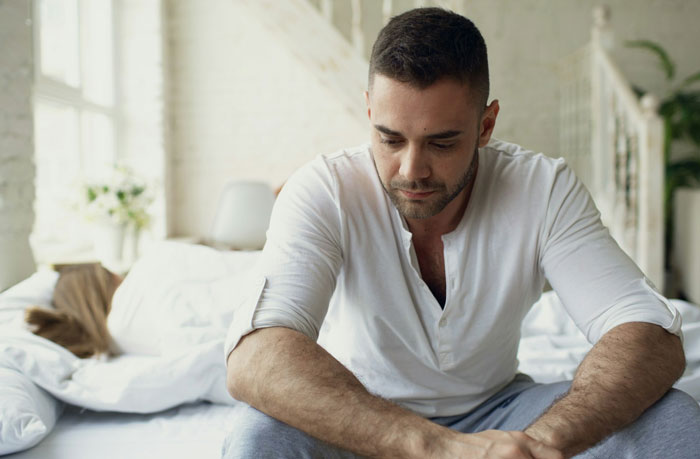 Man looking thoughtful and peaceful sitting on bed after calling out cheater's baby lie from ex relationship trap.