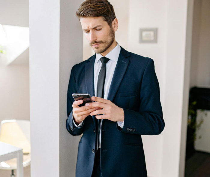 Man in a dark suit reading a message on his phone, reflecting on a cheater trying to trap her ex with a baby lie.