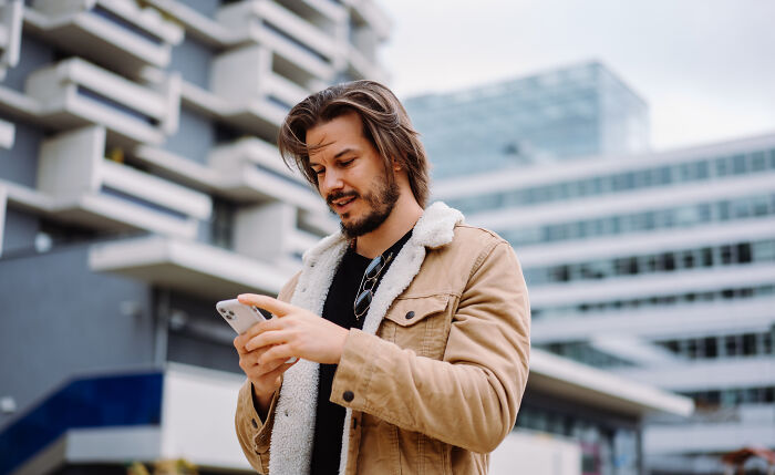 Man in a tan jacket using smartphone outdoors, exploring 24 loopholes to take advantage of in an urban setting.