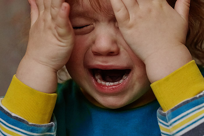 Crying distressed child covering face with hands, representing disruptive kid on a plane upsetting others around.