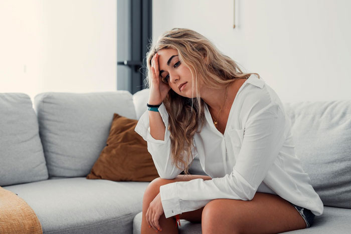Woman looking thoughtful and concerned on a couch, reflecting feelings related to wife plans surgery and family conflict.