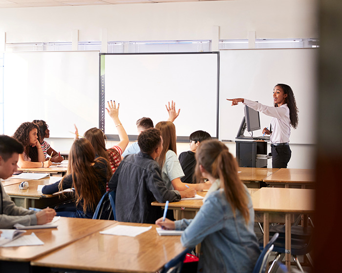 High school teacher engaging with students raising hands in a classroom during a lesson on texting and communication.