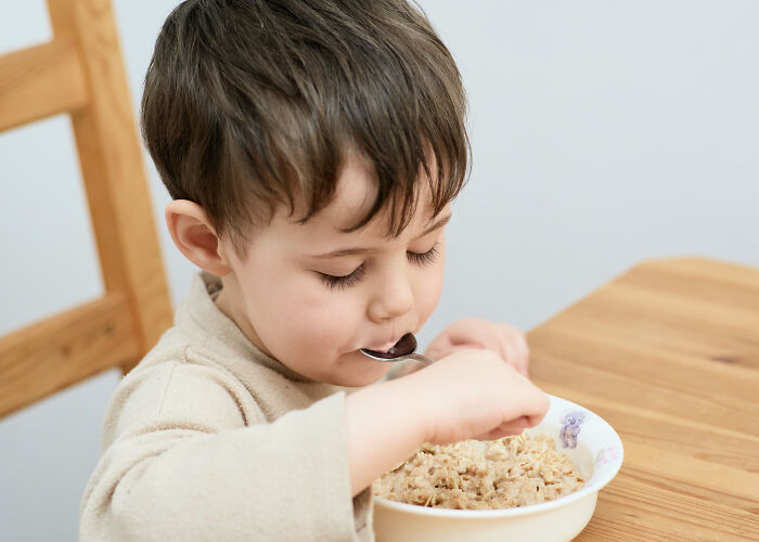 Young boy eating oatmeal at a wooden table, illustrating simple moments amid mysteries once baffling the world now solved.