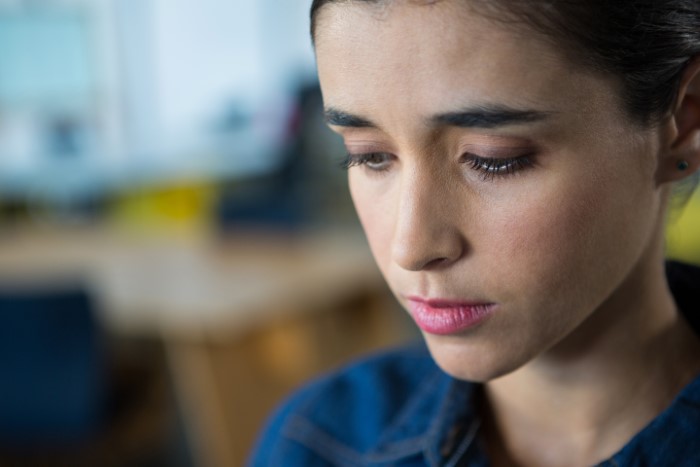 Sad young woman looking down pensively indoors, reflecting on parents lied about food allergies and no contact with daughter.