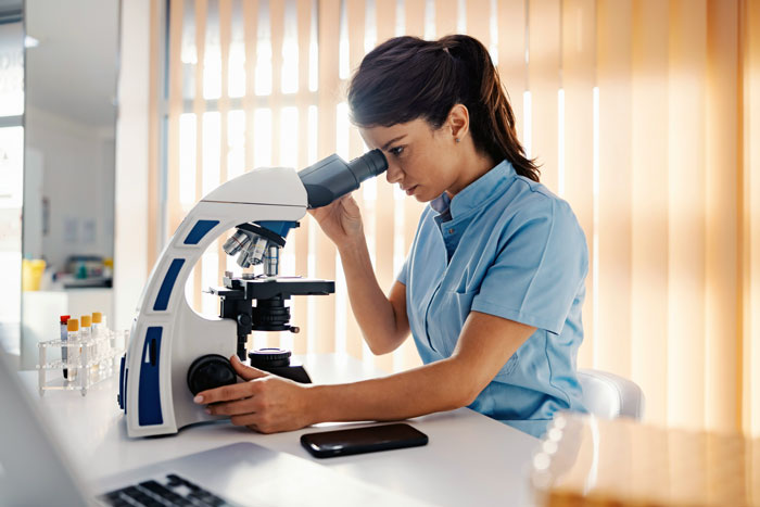 Woman in a lab coat examining samples through a microscope preparing to confront parents about DNA test results Woman in a lab coat examining samples through a microscope preparing to confront parents about DNA test results