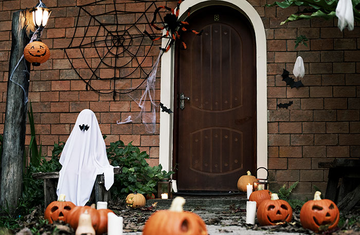 Halloween decor with pumpkins, ghost figures, spider webs, and candles decorating a house porch in festive style.