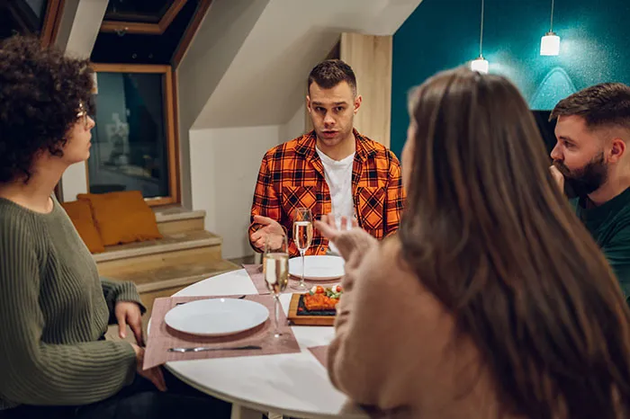 Couple having tense dinner conversation, husband threatening divorce while wife&rsquo;s parents look concerned at table.