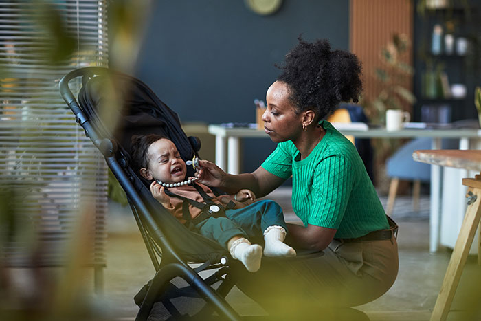 Woman gleams watching cousin&rsquo;s wife struggle with her free babysitter role as baby cries in stroller indoors.