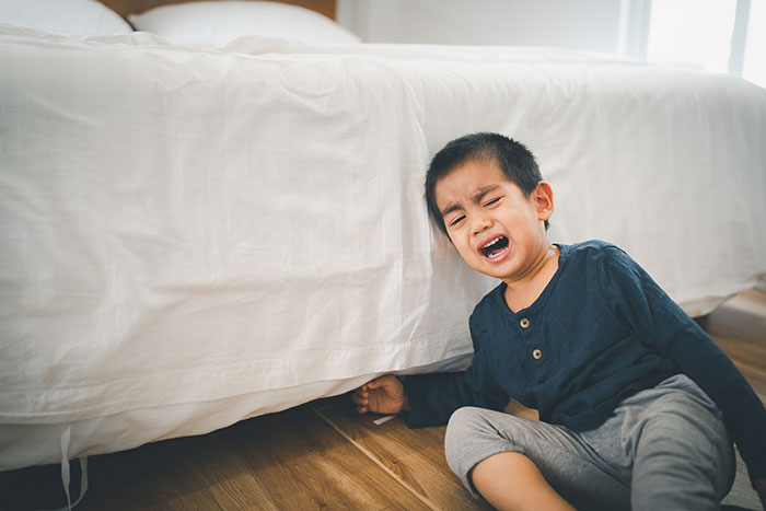 Young boy crying and struggling on the floor near a bed, illustrating babysitter challenges and family struggles.