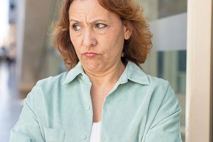 Middle-aged woman with a skeptical expression standing outside, reflecting feelings of being scammed at a show event.