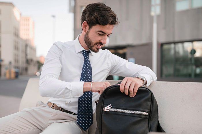 Man in white shirt and tie snooping around in a black purse outdoors, illustrating coworker snoops around in woman&rsquo;s purse scenario.