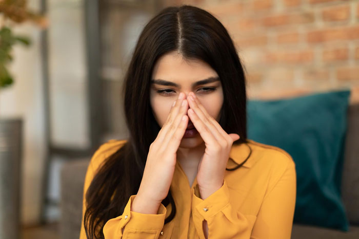 Young woman in a yellow shirt covering her nose, reacting to coworker sensitive smells in an indoor office setting Young woman in a yellow shirt covering her nose, reacting to coworker sensitive smells in an indoor office setting