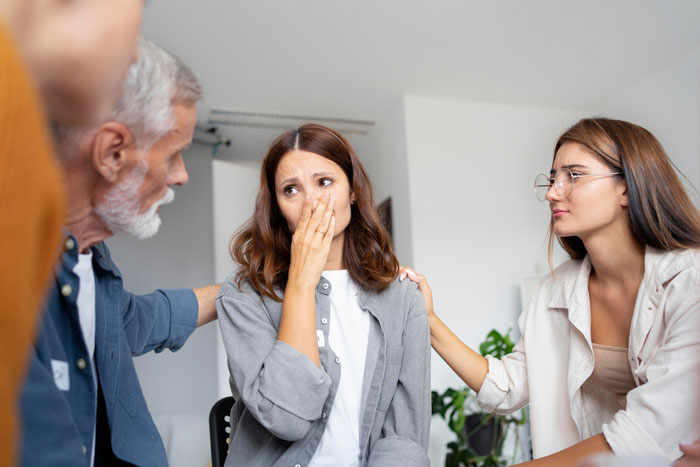 A woman covers her nose reacting to coworker sensitive smells while colleagues offer comfort in an office setting. A woman covers her nose reacting to coworker sensitive smells while colleagues offer comfort in an office setting.