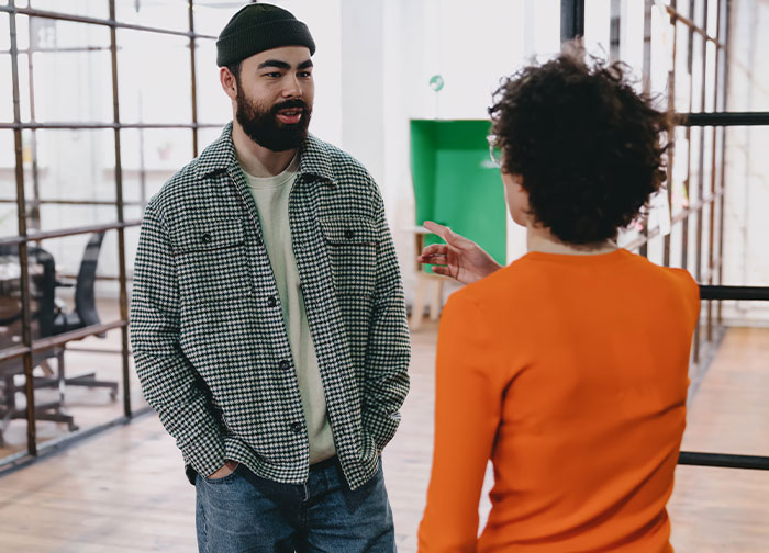 Man asks coworker about wearing makeup daily while they talk in a bright modern office environment.