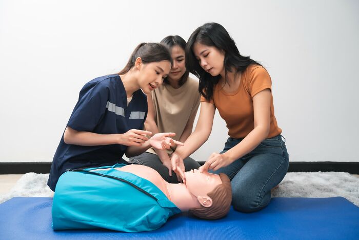 Three women practicing first aid on a training dummy, focusing on simple car stuff skills with minimal training required.