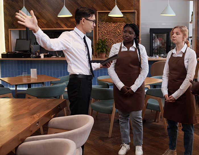 Restaurant manager addressing two employees wearing aprons, illustrating a scene of work nepotism complaints.