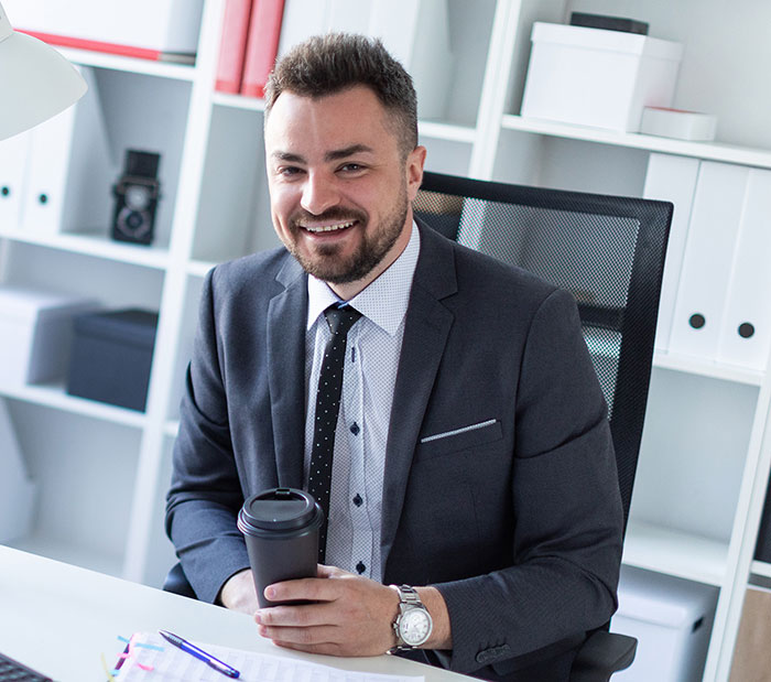 Man in a suit smiling at desk holding coffee cup, representing work nepotism in a professional office setting.