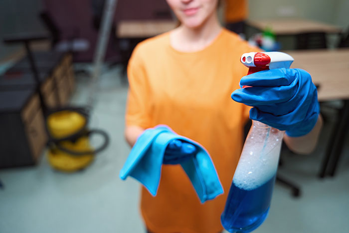 Person in gloves holding spray bottle and cloth, representing work nepotism in cleaning or maintenance jobs.