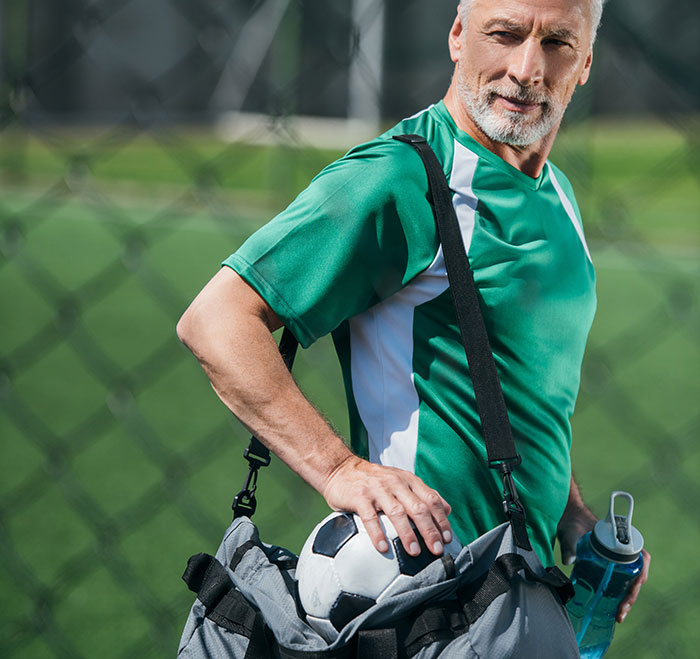 Older man with sports bag holding a soccer ball and water bottle, symbolizing work nepotism in a casual outdoor setting