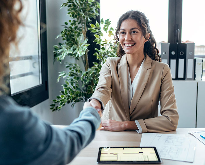 Young woman in a beige blazer smiling and shaking hands during a job interview about work nepotism in an office.