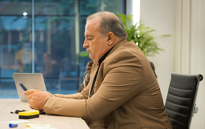 Middle-aged man in a brown jacket using smartphone in an office setting, illustrating work nepotism in the workplace.