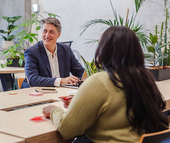 Two colleagues in a modern office discussing work nepotism cases during a casual meeting with plants around.
