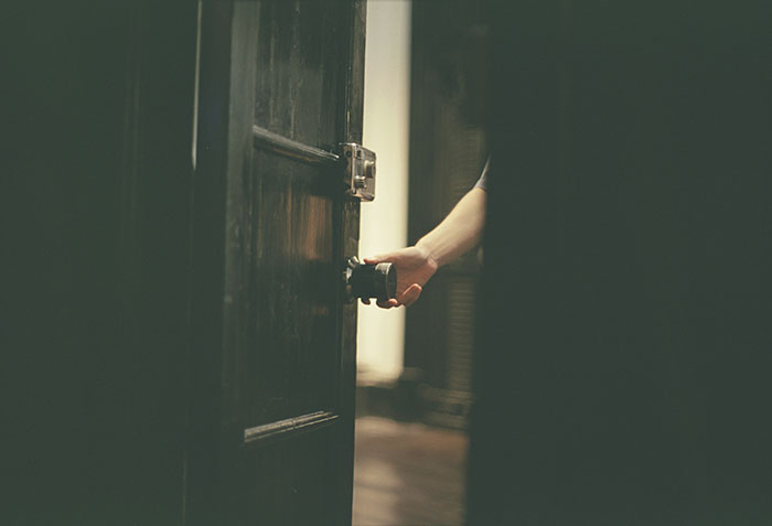 Hand opening a dark door in dim light, evoking spooky urban legends from cities around the world for Halloween.