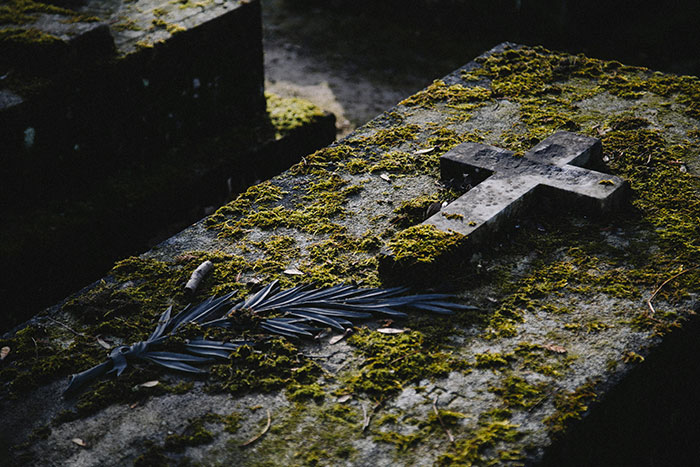 Moss-covered old grave with a stone cross and dark foliage, evoking spooky urban legends and eerie city tales.