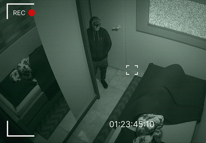 Creepy found footage showing a person in a hoodie standing in a dimly lit room captured by a security camera.