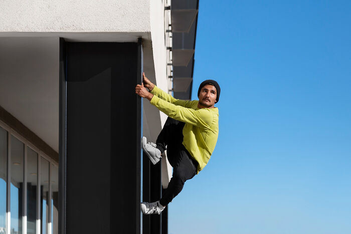 Man wearing a yellow jacket and black beanie climbing the side of a modern building, creating a creepy thing home stories vibe.