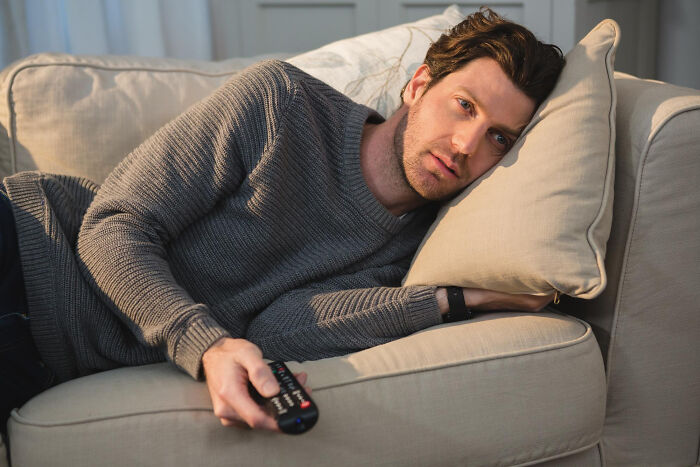 Man lying on couch holding remote, looking unsettled, illustrating a creepy thing in home stories atmosphere.