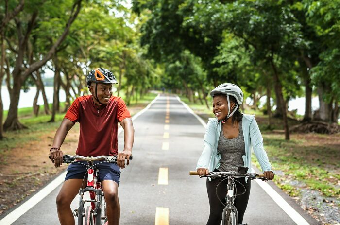 Two people smiling while riding bicycles on a tree-lined road, illustrating simple car stuff skills and maintenance ideas.